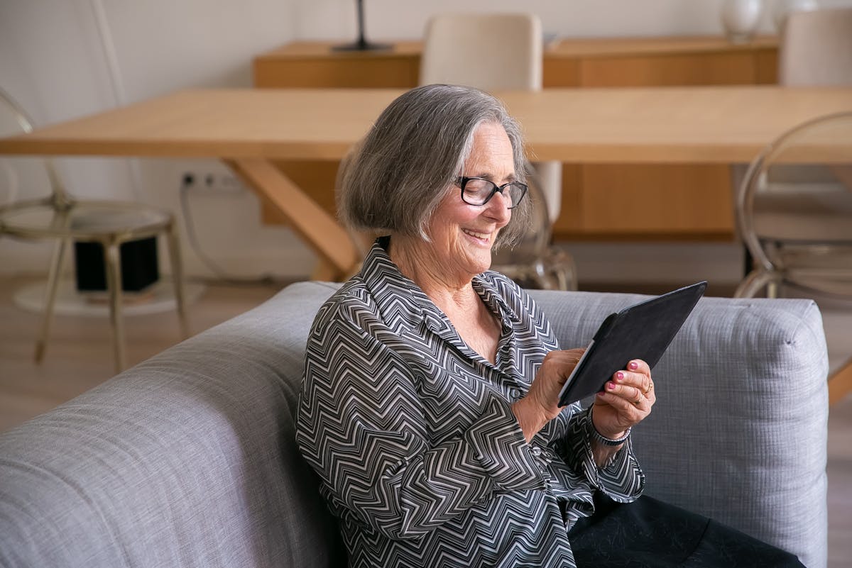 A friendly senior woman smiling warmly while looking at her tablet at home