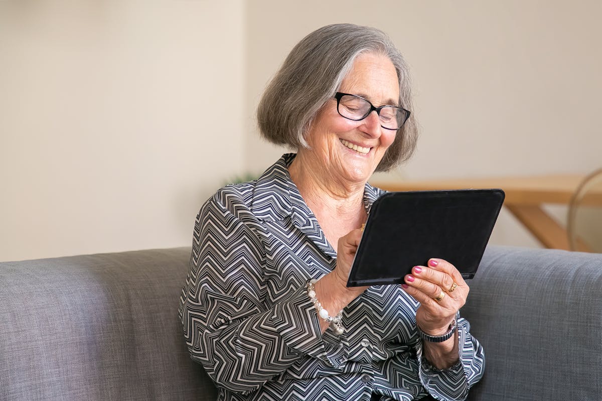 A senior woman smiling while browsing an app on her tablet, representing easy and safe online ordering from home